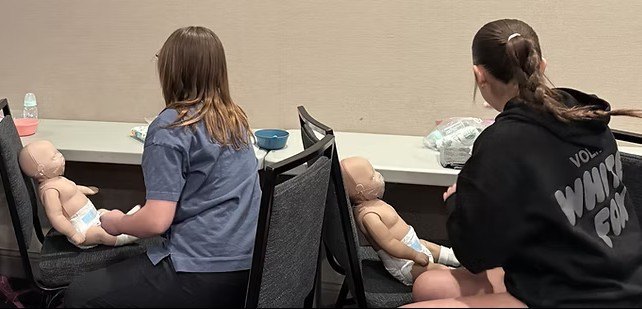 Teen students practicing infant care on training manikins in a Babysitter Essentials class